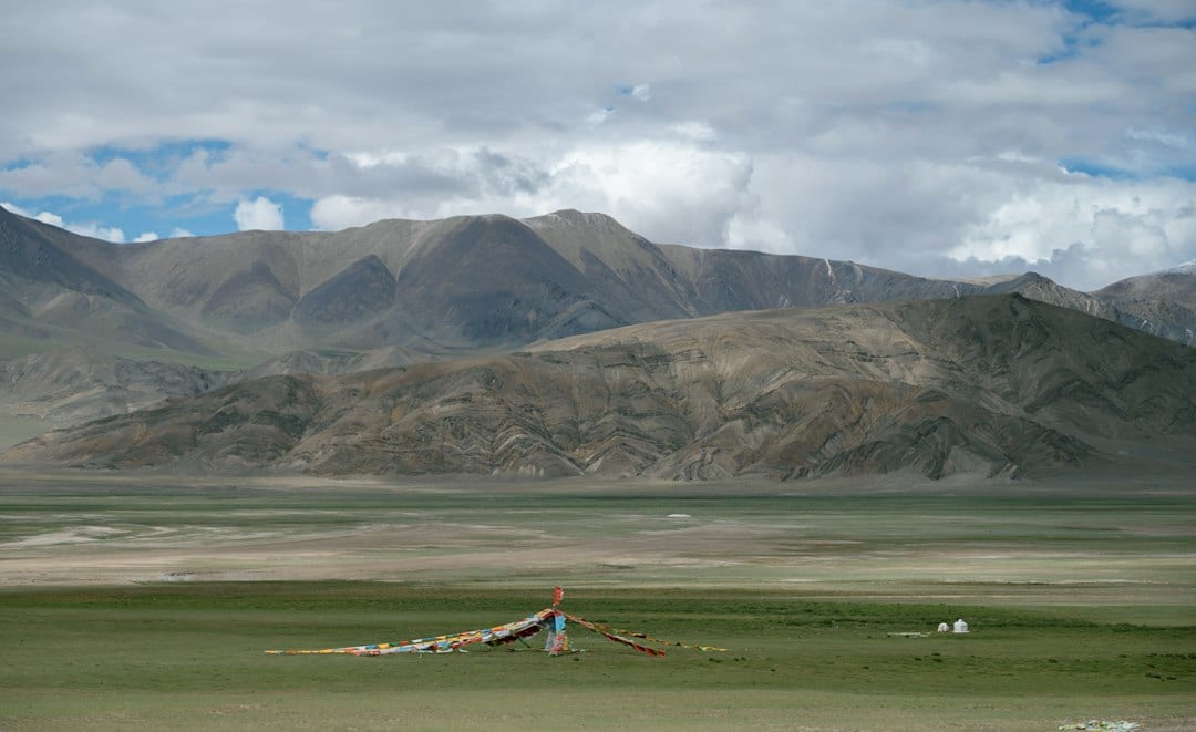Tibetan grassland plateau landscape with prayer flags and barren mountains